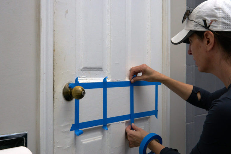 Hands creating blue tape squares on painted door