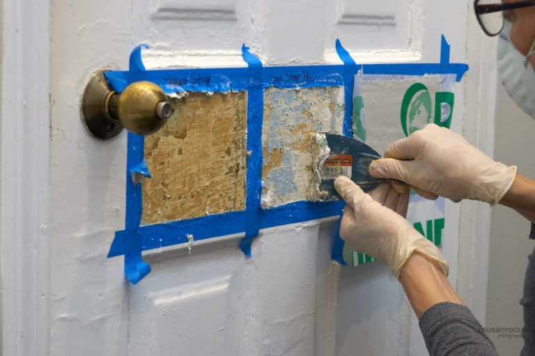 Hands scraping paint from one of three test patches on painted bath door